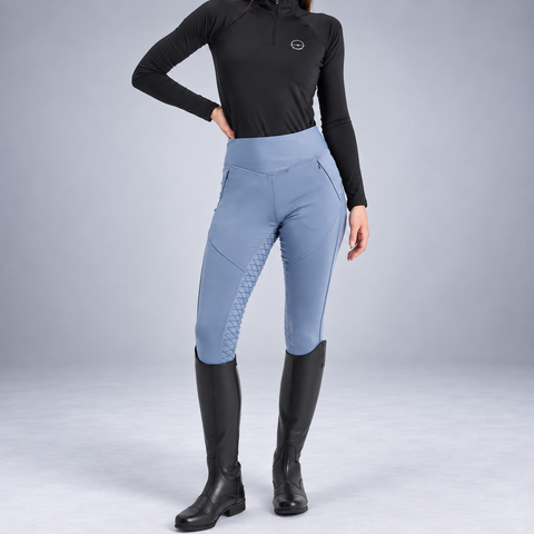 Ocean blue full seat riding tights with zip phone pocket, worn with tall boots